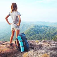 Woman at top of mountain with backpack, looking out at picturesque valley